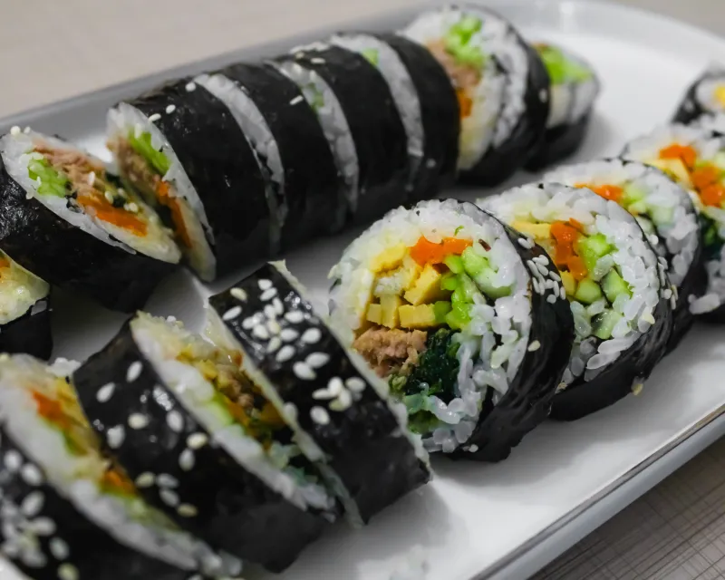 Close-up of sliced gimbap rolls filled with egg, carrot, cucumber and greens on a white plate