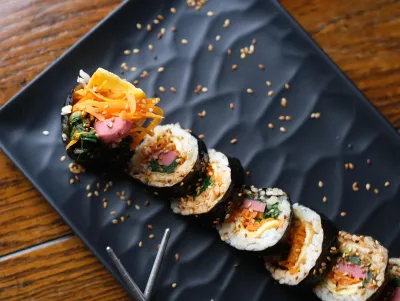 Sesame-topped gimbap rolls lined up on a black wavy tray