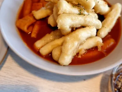 Plate of tteokbokki rice cakes in red sauce topped with crispy battered pieces