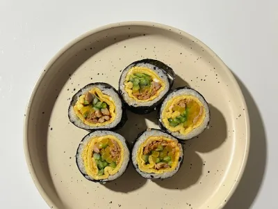 Sliced gimbap rolls with egg and vegetable filling on a round beige plate