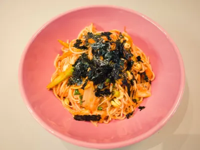 Pink bowl of cold spicy noodles topped with shredded seaweed