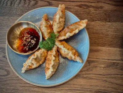 Pan-fried dumplings arranged on a blue plate with a small bowl of dipping sauce