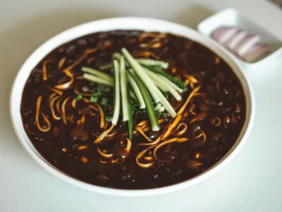 Bowl of jjajangmyeon noodles in black bean sauce topped with sliced cucumber