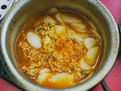 Metal pot of rice cakes and ramen noodles in an orange broth